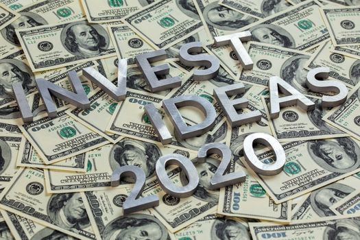 The words INVEST IDEAS 2020 laid with metal letters on the US dollar bills background - with selective focus and diagonal composition.