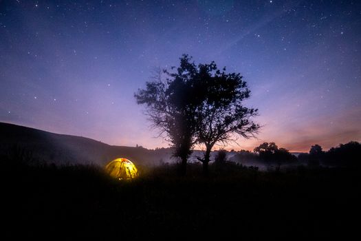 yellow tent under tree at summer starry night with fog.