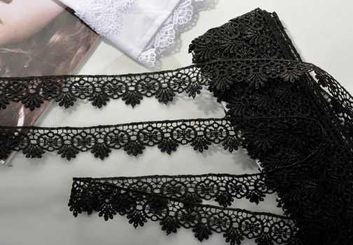 Tapes of black gentle guipure, beauty lace fabric on light background. Elastic material. Using for Atelier and needlework store.