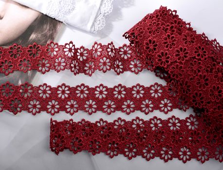 Tapes of red vinous gentle guipure, beauty silk lace fabric on light background. Elastic material. Using for Atelier and needlework store. Flat lay style