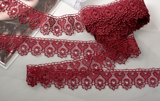 Tapes of red vinous gentle guipure, beauty silk lace fabric on light background. Elastic material. Using for Atelier and needlework store. Flat lay style