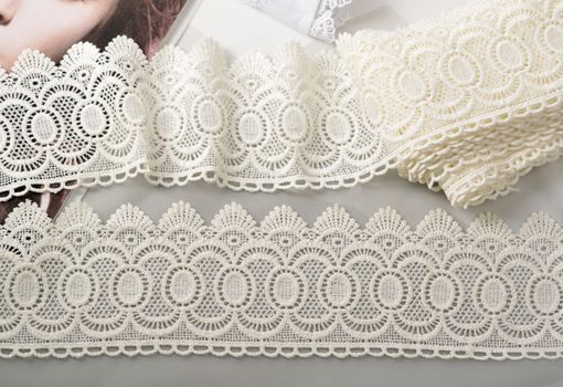 Tapes of ecru white guipure, beauty silk lace fabric on light background. Elastic material. Using for Atelier and needlework store. Flat lay style