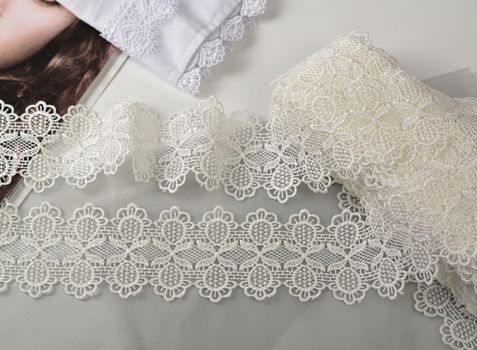 Tapes of ecru white guipure, beauty silk lace fabric on light background. Elastic material. Using for Atelier and needlework store. Flat lay style