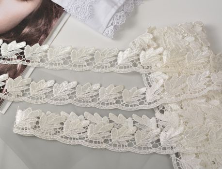Tapes of ecru white guipure, beauty silk lace fabric on light background. Elastic material. Using for Atelier and needlework store. Flat lay style