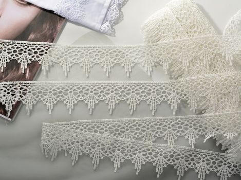 Tapes of ecru white guipure, beauty silk lace fabric on light background. Elastic material. Using for Atelier and needlework store. Flat lay style