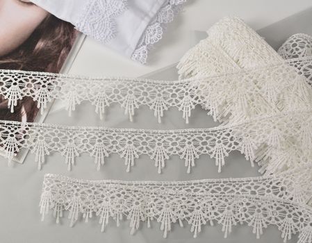 Tapes of ecru white guipure, beauty silk lace fabric on light background. Elastic material. Using for Atelier and needlework store. Flat lay style