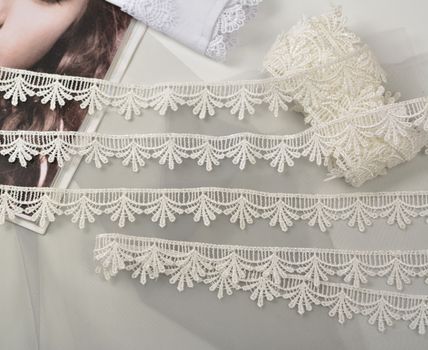 Tapes of ecru white guipure, beauty silk lace fabric on light background. Elastic material. Using for Atelier and needlework store. Flat lay style