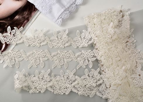 Tapes of ecru white guipure, beauty silk lace fabric on light background. Elastic material. Using for Atelier and needlework store. Flat lay style