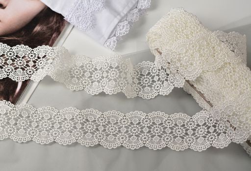 Tapes of ecru white guipure, beauty silk lace fabric on light background. Elastic material. Using for Atelier and needlework store. Flat lay style