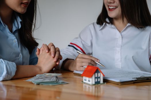 Cropped image of real estate agent assisting client to sign contract paper at desk with house model.