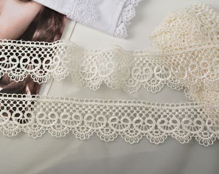 Tapes of ecru white guipure, beauty silk lace fabric on light background. Elastic material. Using for Atelier and needlework store. Flat lay style