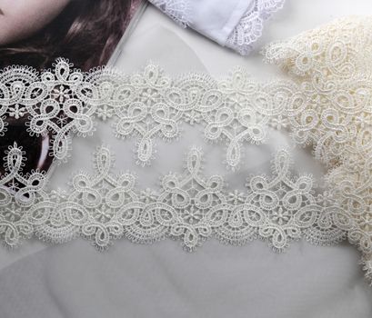 Tapes of ecru white guipure, beauty silk lace fabric on light background. Elastic material. Using for Atelier and needlework store. Flat lay style