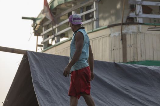 Jakarta, Sunda Kelapa Port, Indonesia - July 15, 2019: A man inspects the cargo of a ship in the port of Jakarta, protecting it from the sun and humidity before leaving.