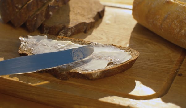 Close up hand smearing bread with butter on a wooden cutting board