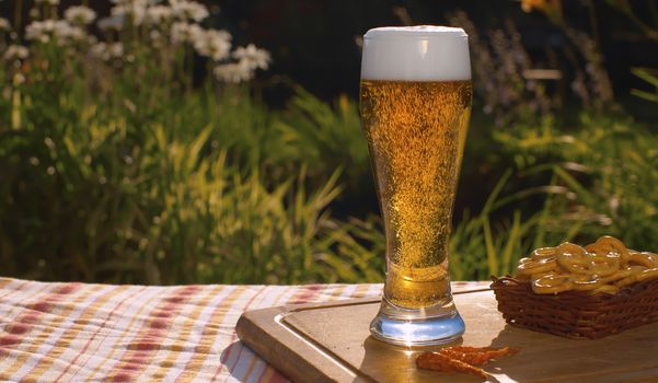 Close up glass of cold light beer on the table outdoors. Foamy sparkling gold drink on natural background in the garden