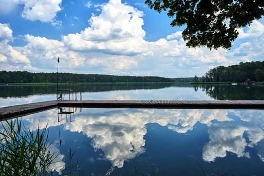 Wooden pier and reflection of clouds in the waters of Lake Chycina in Poland