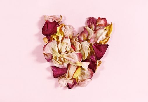 Beautiful heart shape made with pink , red , yellow petals on pink background 