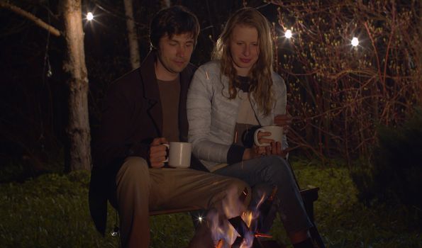 Young happy couple at night sitting near campfire. Family on weekend in the woods
