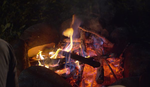 Close up bonfire in the forest at night. Burning woods and stones on the grass glade. Concept of traveling and healthy lifestyle