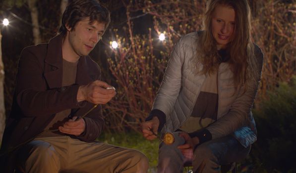 Close up bonfire. Young happy couple at night roasting marshmallow on campfire. Family on weekend in the forest. Healthy lifestyle concept