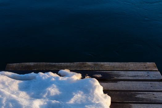 wooden pier with snow on dark water background.