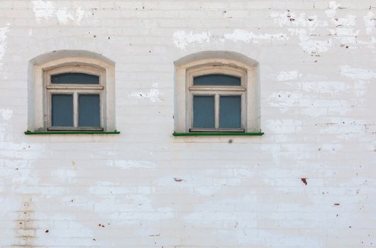 two windows in thick brick mediewal wall under worn layer of white plaster.