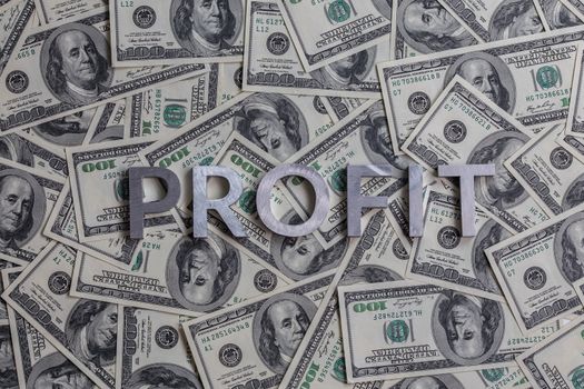 The word PROFIT laid with aluminium letters on the US dollar banknotes background - with selective focus.