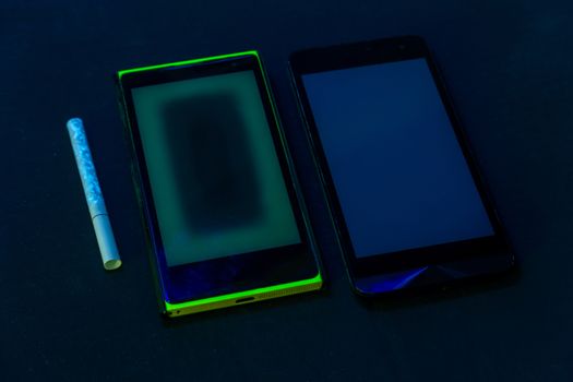 used phones and cigarette under UV light on black bckground with selective focus.