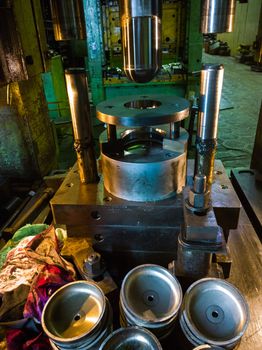 dirty used low tech stamping press producing round aliminium parts in dark environment.