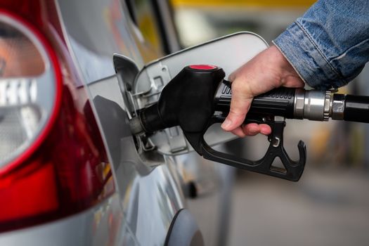 hand in jeans jacket refueling gray metallic car on gas station - closeup with selective focus and blur