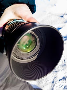 A telephoto dslr camera lens with dew sweating and snow at outdoor winter photoshoot. Real life situation with part of hand, holding camera.
