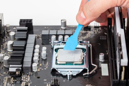 hand applies gray thermal grease on central processor unit in pc motherboard - closeup with selective focus and blur