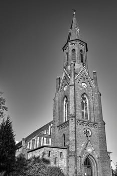The tower of the historic, neo-Gothic red brick church in the village of Sokola Dabrowa in Poland, black and white
