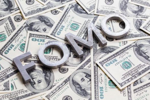 The word FOMO - fear of missing out - laid with aluminium letters on the US dollar banknotes background - with selective focus and diagonal composition.