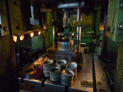 dirty used low tech stamping press producing round aliminium parts in dark environment.