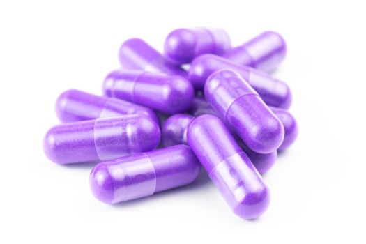 pile of proton purple color organic capsules isolated on white background closeup with selective focus.