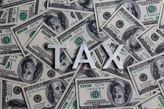 The words TAX laid with metal letters on the US dollar bills background - with selective focus and diagonal composition.