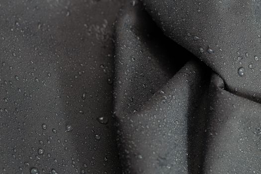 dark gray waterproof hydrophobic crumpled cloth closeup with water drops selective focus background.