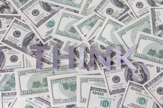 The word THINK laid with aluminium letters on the US dollar banknotes background - with selective focus and blur.