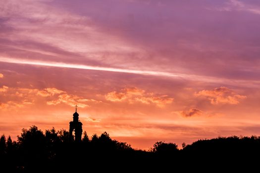 black silhouette of church and forest horizon on golden-purple sunset sky with soft clouds.