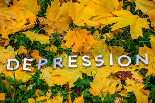 The word DEPRESSION laid with aluminium thick letters on the ground with maple leaves, green grass and copyspace. Fall season illness symbol.