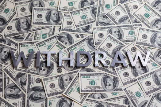 The word WITHDRAW laid with aluminium letters on the US dollar banknotes background - with selective focus and straight composition.