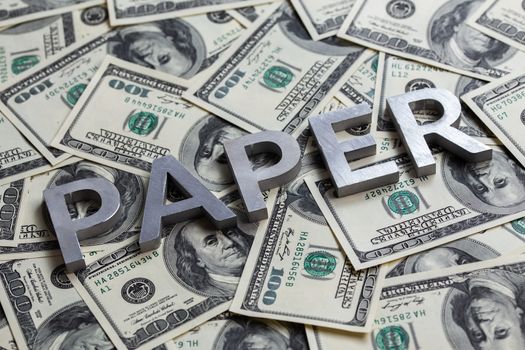 The word PAPER laid with aluminium letters on the US dollar banknotes background - with selective focus.