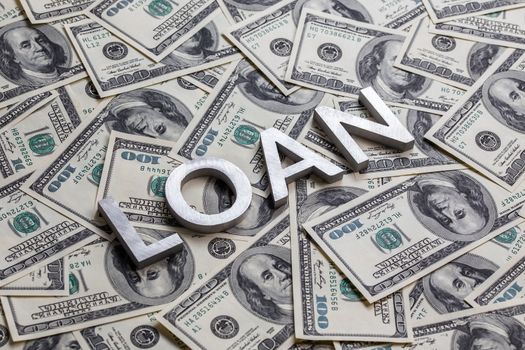 The word LOAN laid with aluminium letters on the US dollar banknotes background - with selective focus and diagonal composition.