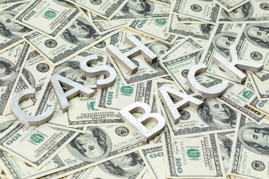 The words CASH BACK laid with aluminium thick letters on the US dollar bills background - with selective focus and diagonal composition.