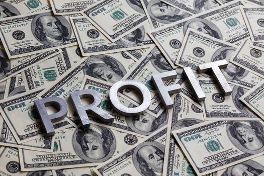 The word PROFIT laid with aluminium letters on the US dollar banknotes background - with selective focus and diagonal composition.