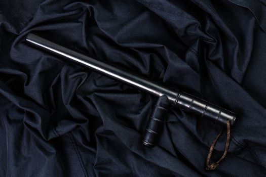 black rubber police baton on black shirt wrinkled cloth low-key flat lay.