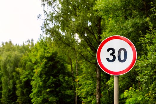 Road sign speed limit 30 kilometers per hour on green forest background with selective focus. End of youth symbol too. Horizontal orientation.