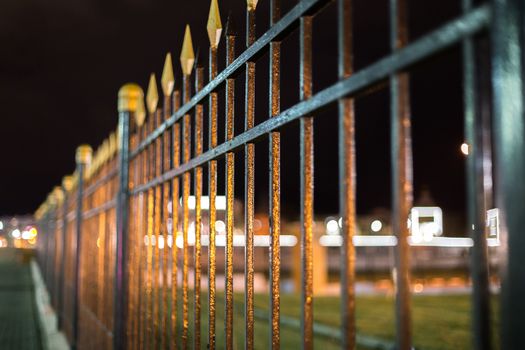 black iron forged fence at night with selective focus and boke blur and reflections.
