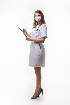 Slender nurse in medical dress and medical mask records data on white background